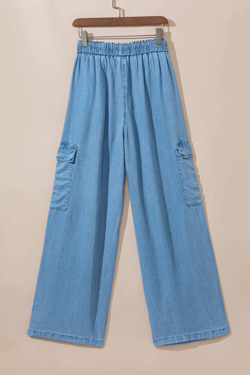 Back view of wide-leg denim pants hanging on wooden hanger with visible back seams and cargo pockets at Tela Designs store