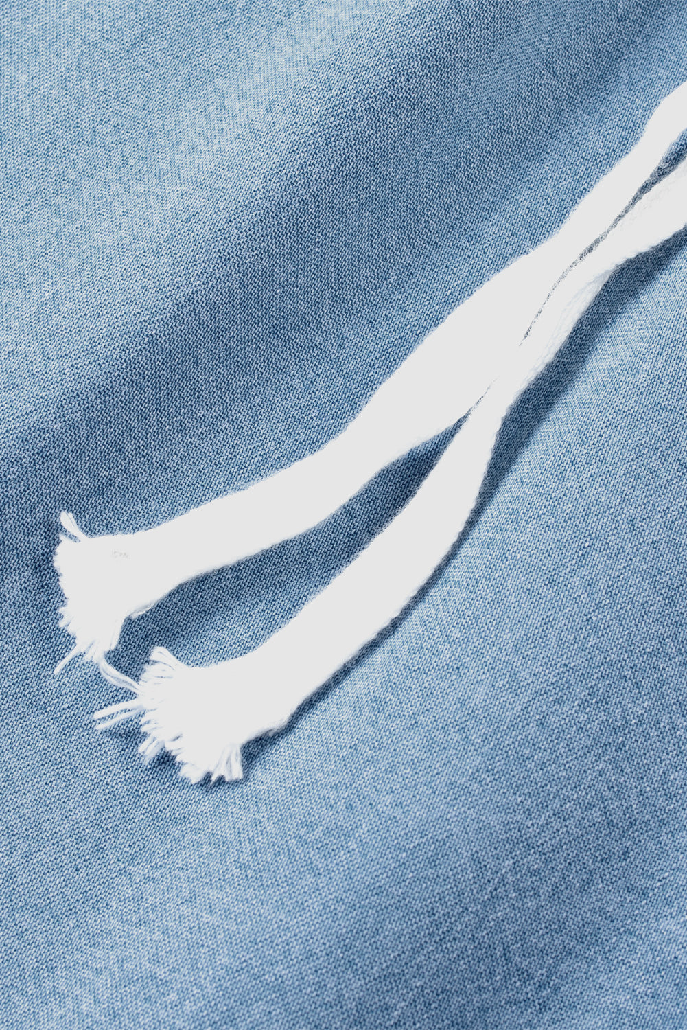Macro shot of white drawstring cord laid over light blue denim fabric texture at Tela Designs Store