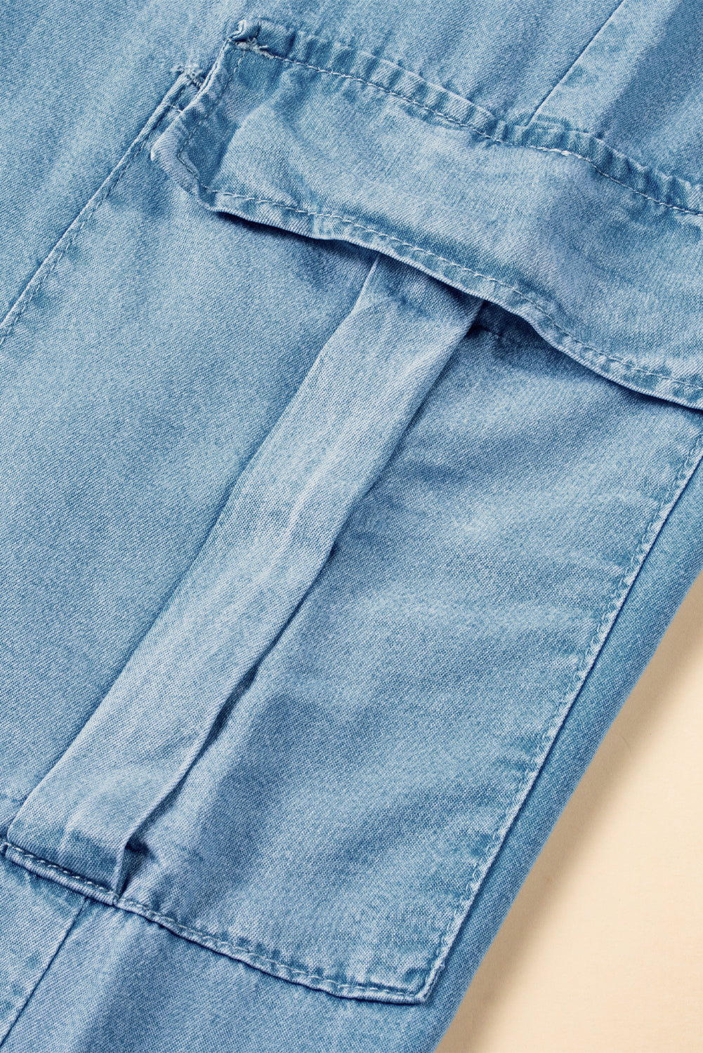 Close-up of utility cargo pocket on light blue denim pants with flap and stitched seam at Tela Designs Store