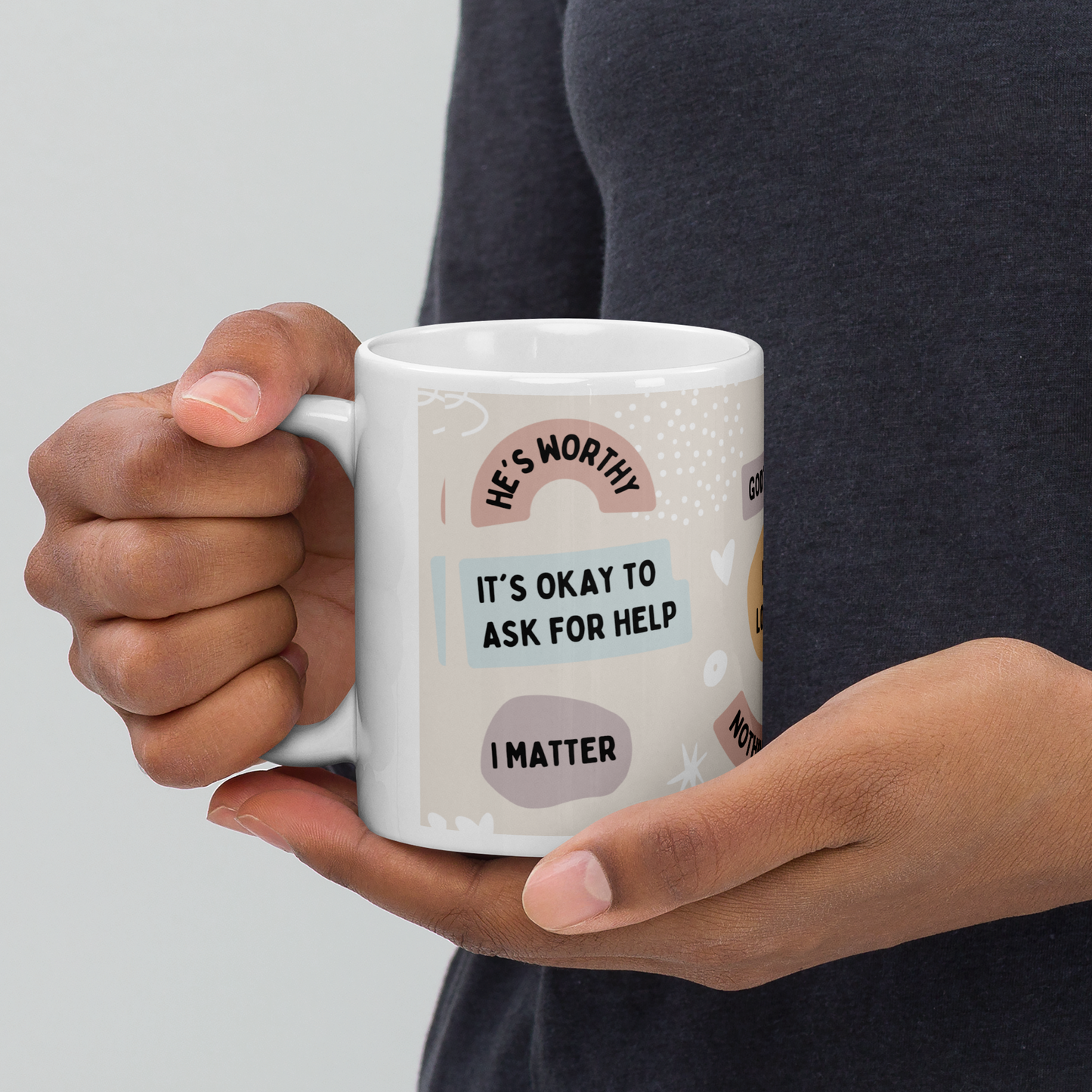 A woman of color shown holding a white ceramic mug in her hands, cupping it that has Christian affirmations printed on it, such as 'I'm grateful' and 'He hears and answers me' (left view). by Tela Designs Store.