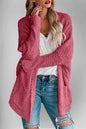 A woman wearing a pink, pocketed, open-front cardigan with long sleeves over a white top and blue jeans.