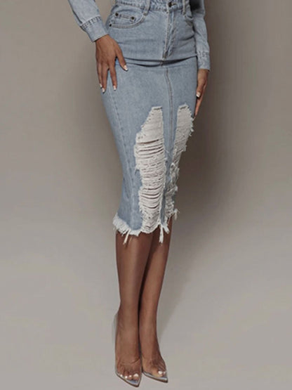 Woman wearing high-waisted distressed denim midi skirt with frayed hem and front slit, styled with clear heels at Tela Desigs Store.