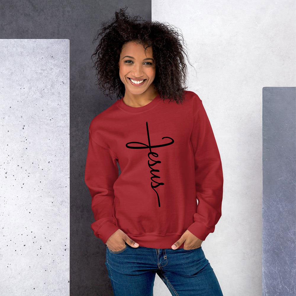 Smiling African American woman with wavy afro wearing red JESUS script sweatshirt and jeans.