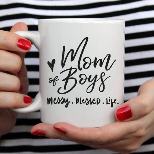 A close-up of a white ceramic mug with the phrase “Mom of Boys. Messy. Blessed. Life.” 